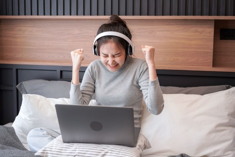 Woman in bed celebrating while on her laptop